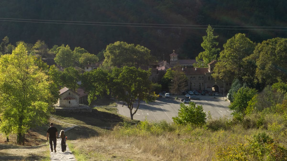 Man and child walking towards Bachkovo Monastery in Bulgaria surrounded by lush greenery.